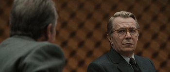 Movie still from “Tinker Tailor Soldier Spy” (2011), directed by Tomas Alfredson – A man in a suit and glasses talking to another man; Close Up shot, Over the shoulder angle