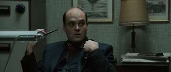 Movie still from “Tinker Tailor Soldier Spy” (2011), directed by Tomas Alfredson – A man in a suit and tie with a chain around his neck; Close Up shot, Over the shoulder angle
