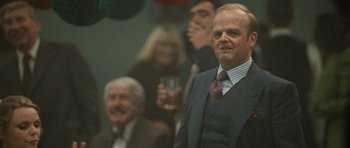 Movie still from “Tinker Tailor Soldier Spy” (2011), directed by Tomas Alfredson – A man standing in front of a group of people; Close Up shot, Over the shoulder angle