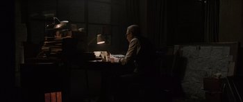 Movie still from “Tinker Tailor Soldier Spy” (2011), directed by Tomas Alfredson – An older man sitting at a desk in a dark room; Wide shot, High angle