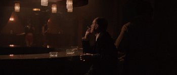 Movie still from “Tinker Tailor Soldier Spy” (2011), directed by Tomas Alfredson – A man sitting at a table smoking a cigarette; Medium shot, Over the shoulder angle