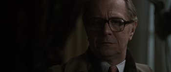 Movie still from “Tinker Tailor Soldier Spy” (2011), directed by Tomas Alfredson – An older man wearing glasses and a suit; Close Up shot, Over the shoulder angle