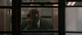 An older man talking on a cell phone through a window