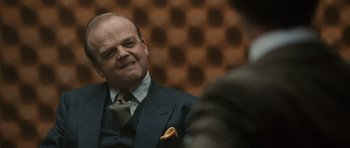 Movie still from “Tinker Tailor Soldier Spy” (2011), directed by Tomas Alfredson – A man wearing a suit and tie in front of an audience; Close Up shot, Over the shoulder angle