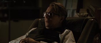 Movie still from “Tinker Tailor Soldier Spy” (2011), directed by Tomas Alfredson – A man sitting in a chair with glasses on his face; Close Up shot, Over the shoulder angle