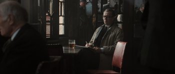 Movie still from “Tinker Tailor Soldier Spy” (2011), directed by Tomas Alfredson – A man sitting at a table with a glass of beer; Medium shot, Over the shoulder angle