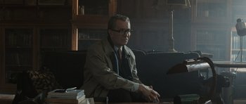 Movie still from “Tinker Tailor Soldier Spy” (2011), directed by Tomas Alfredson – An older man sitting at a table in front of books; Medium shot, Over the shoulder angle