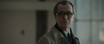 Movie still from “Tinker Tailor Soldier Spy” (2011), directed by Tomas Alfredson – A person wearing glasses and a coat; Close Up shot, Over the shoulder angle