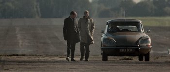Movie still from “Tinker Tailor Soldier Spy” (2011), directed by Tomas Alfredson – Two men are standing in front of a car; Wide shot, Over the shoulder angle