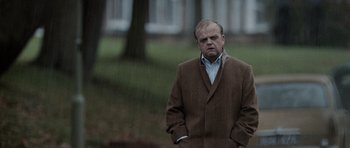 Movie still from “Tinker Tailor Soldier Spy” (2011), directed by Tomas Alfredson – A man in a brown coat is standing in the rain; Medium shot, Low angle