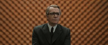 Movie still from “Tinker Tailor Soldier Spy” (2011), directed by Tomas Alfredson – A man wearing a suit and tie in front of an orange wall; Medium shot, Low angle