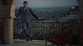 Movie still from “To Catch a Thief” (1955), directed by Alfred Hitchcock – A man in a suit and tie standing next to a railing; Wide shot, High angle