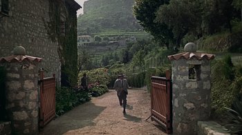 Movie still from “To Catch a Thief” (1955), directed by Alfred Hitchcock – A man walking down a dirt road near a lush green hillside; Extreme Wide shot, High angle