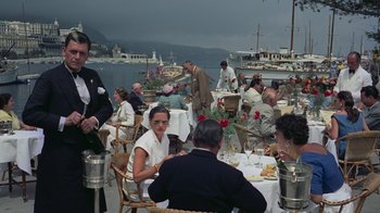 Movie still from “To Catch a Thief” (1955), directed by Alfred Hitchcock – A group of people sitting at a table near a body of water; Wide shot, High angle