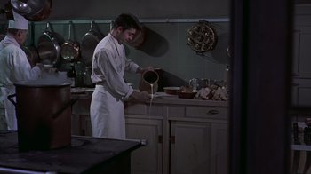 Movie still from “To Catch a Thief” (1955), directed by Alfred Hitchcock – A man in a kitchen preparing a meal; Medium shot, High angle
