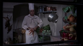Movie still from “To Catch a Thief” (1955), directed by Alfred Hitchcock – A man wearing a chef's hat in a kitchen; Medium shot, Over the shoulder angle