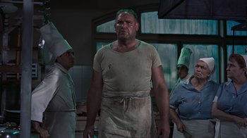 Movie still from “To Catch a Thief” (1955), directed by Alfred Hitchcock – A man in a white shirt and apron standing in a kitchen; Medium shot, Low angle