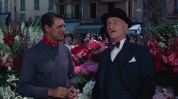 Movie still from “To Catch a Thief” (1955), directed by Alfred Hitchcock – A man in a suit and a man in a hat standing next to each other in front of flowers; Medium shot, Over the shoulder angle