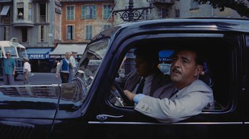 Movie still from “To Catch a Thief” (1955), directed by Alfred Hitchcock – Two men in a black car driving down a street; Medium shot, High angle