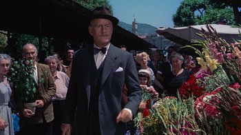 Movie still from “To Catch a Thief” (1955), directed by Alfred Hitchcock – An older man in a suit and hat is walking through a flower market; Medium shot, Low angle