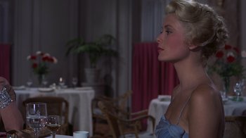 Movie still from “To Catch a Thief” (1955), directed by Alfred Hitchcock – A woman sitting at a table with a glass of wine in front of her; Medium shot, Over the shoulder angle