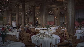 Movie still from “To Catch a Thief” (1955), directed by Alfred Hitchcock – A man standing in front of a room filled with tables and chairs; Extreme Wide shot, High angle