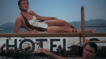 Movie still from “To Catch a Thief” (1955), directed by Alfred Hitchcock – A woman sitting on the ground next to a hotel sign; Wide shot, Overhead angle