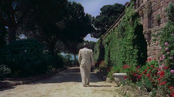 Movie still from “To Catch a Thief” (1955), directed by Alfred Hitchcock – A man walking down a dirt path near a garden; Wide shot, High angle