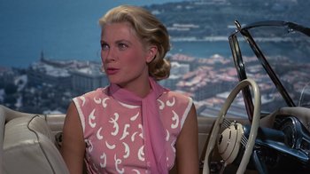 Movie still from “To Catch a Thief” (1955), directed by Alfred Hitchcock – A woman sitting in a car wearing a pink dress; Medium shot, High angle