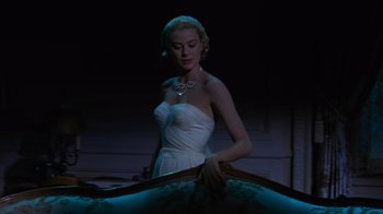 Movie still from “To Catch a Thief” (1955), directed by Alfred Hitchcock – A woman in a white dress standing in front of a table; Medium shot, Low angle