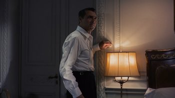 Movie still from “To Catch a Thief” (1955), directed by Alfred Hitchcock – A man leaning against a wall in front of a lamp; Medium shot, Low angle