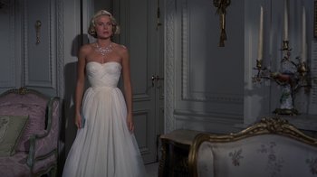 Movie still from “To Catch a Thief” (1955), directed by Alfred Hitchcock – A woman in a white dress standing in front of a chair; Medium shot, High angle