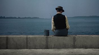 Movie still from “To Catch a Thief” (1955), directed by Alfred Hitchcock – A man sitting on a wall with a fishing pole; Wide shot, High angle