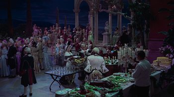 Movie still from “To Catch a Thief” (1955), directed by Alfred Hitchcock – A group of people standing around a table with food on top of it; Wide shot, High angle