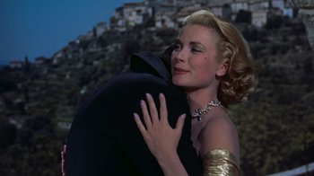 Movie still from “To Catch a Thief” (1955), directed by Alfred Hitchcock – A beautiful blonde woman hugging a man in a black suit; Medium shot, Low angle