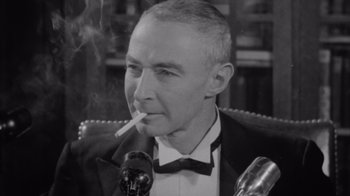 Movie still from “To End All War: Oppenheimer & the Atomic Bomb” (2023), directed by Christopher Cassel – An older man smoking a cigarette in front of a microphone; Close Up shot, Low angle