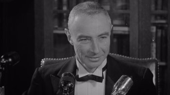 Movie still from “To End All War: Oppenheimer & the Atomic Bomb” (2023), directed by Christopher Cassel – An older man in a suit and bow tie is smiling; Close Up shot, High angle