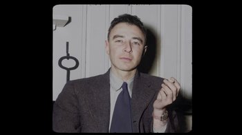 Movie still from “To End All War: Oppenheimer & the Atomic Bomb” (2023), directed by Christopher Cassel – A man wearing a suit and tie holding a cigarette; Medium shot, High angle