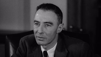 Movie still from “To End All War: Oppenheimer & the Atomic Bomb” (2023), directed by Christopher Cassel – An old black and white photo of a man in a suit and tie; Close Up shot, Low angle