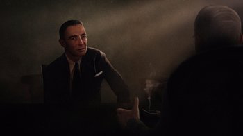 Movie still from “To End All War: Oppenheimer & the Atomic Bomb” (2023), directed by Christopher Cassel – A man sitting at a table with a cup of coffee; Medium shot, Over the shoulder angle