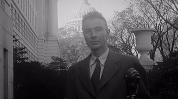 Movie still from “To End All War: Oppenheimer & the Atomic Bomb” (2023), directed by Christopher Cassel – A black and white photo of a man in a suit and tie in front of the capitol building; Close Up shot, Low angle