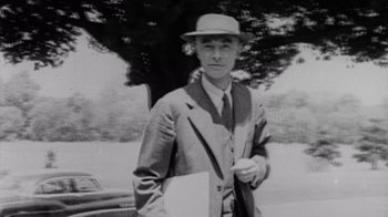 Movie still from “To End All War: Oppenheimer & the Atomic Bomb” (2023), directed by Christopher Cassel – An old photo of a man wearing a suit and a hat; Medium shot, Low angle