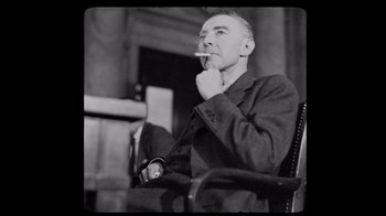 Movie still from “To End All War: Oppenheimer & the Atomic Bomb” (2023), directed by Christopher Cassel – An older man sitting in a chair with a cigarette in his mouth; Medium shot, Low angle