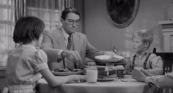 Movie still from “To Kill a Mockingbird” (1962), directed by Robert Mulligan – A man and woman sitting at a table with plates of food on it; Medium shot, Over the shoulder angle