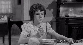 Movie still from “To Kill a Mockingbird” (1962), directed by Robert Mulligan – A young girl sitting at a table eating cake; Medium shot, High angle