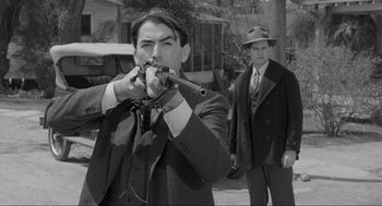 Movie still from “To Kill a Mockingbird” (1962), directed by Robert Mulligan – A man in a suit and tie holding a whip; Medium shot, Over the shoulder angle
