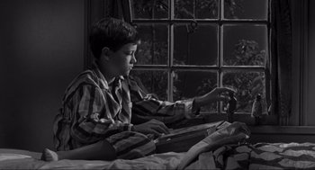 Movie still from “To Kill a Mockingbird” (1962), directed by Robert Mulligan – A young boy sitting on a bed looking at a window; Medium shot, High angle