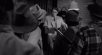 Movie still from “To Kill a Mockingbird” (1962), directed by Robert Mulligan – A man sitting in a chair in front of a group of people; Medium shot, Over the shoulder angle