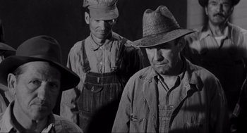 Movie still from “To Kill a Mockingbird” (1962), directed by Robert Mulligan – A black and white photo of two men in overalls and hats; Medium shot, Over the shoulder angle