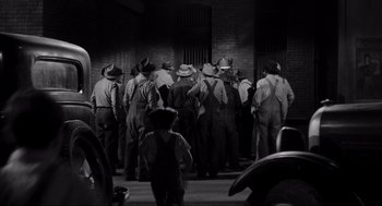 Movie still from “To Kill a Mockingbird” (1962), directed by Robert Mulligan – A group of men standing next to each other on a street; Wide shot, High angle